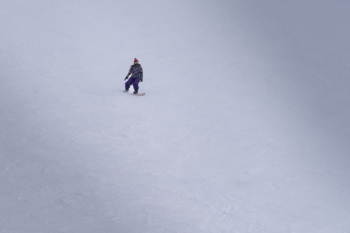 A snowboarder riding down a wide open snowy slope