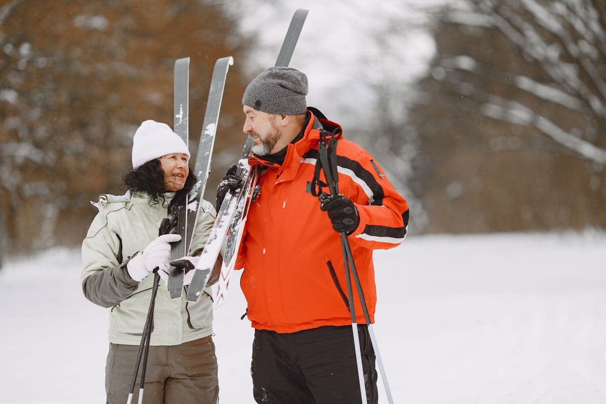 A couple in winter clothing holding their skis on a snowy day
